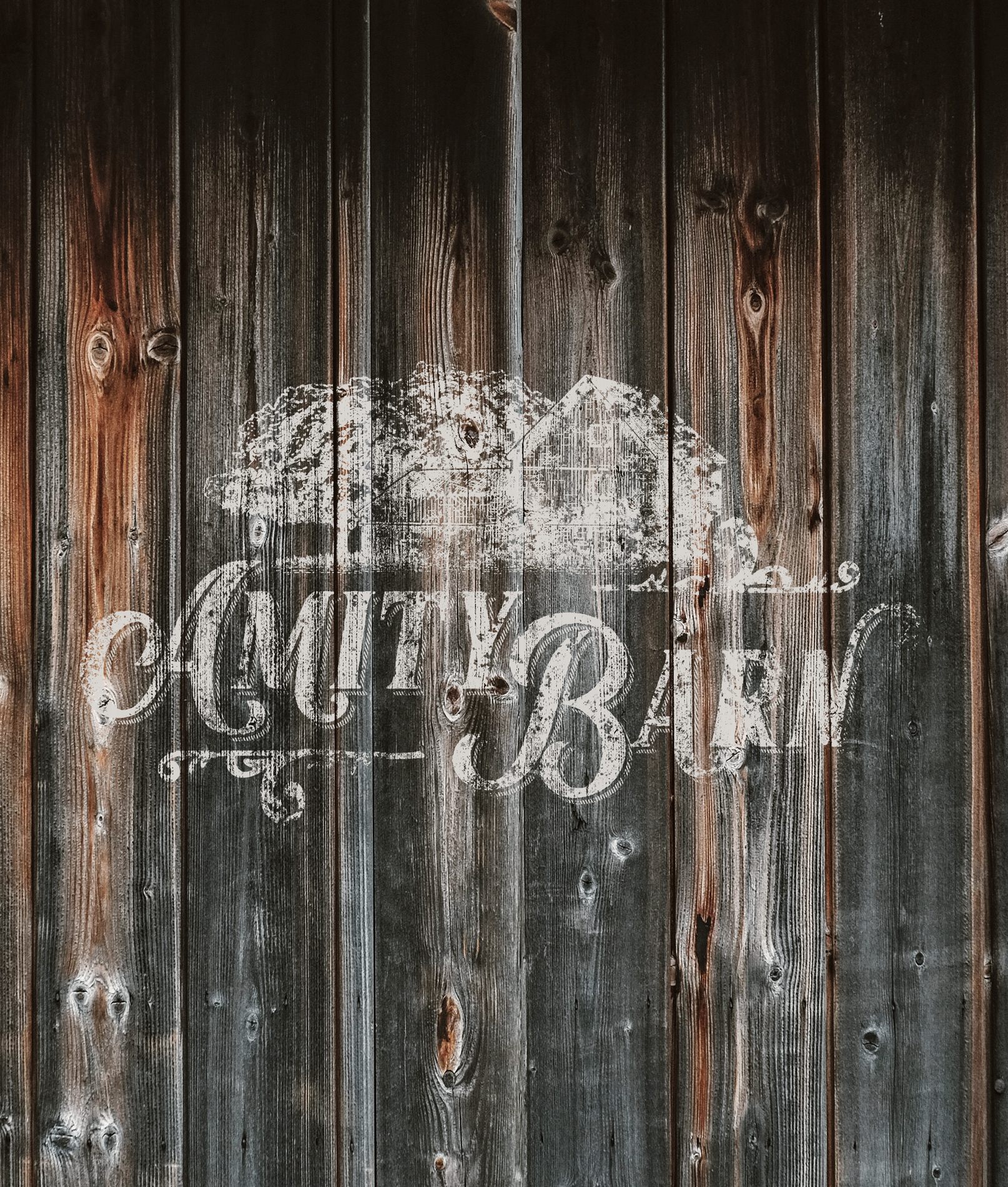 The Amity Barn logo painted in white on weathered barn wood siding