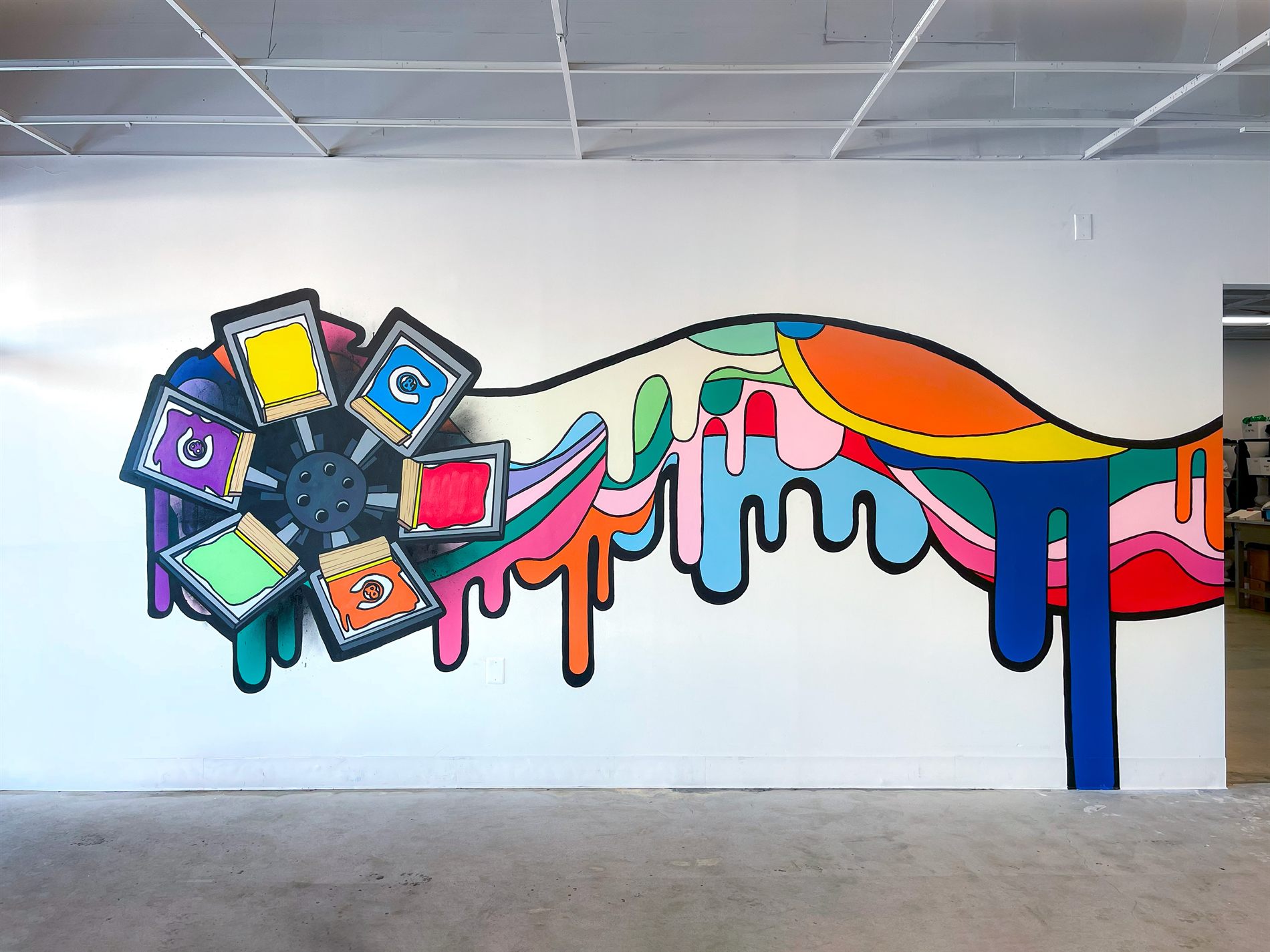 The finished Bolder Outfitters mural, a carousel screen press spilling a wave of colored ink across the shop wall