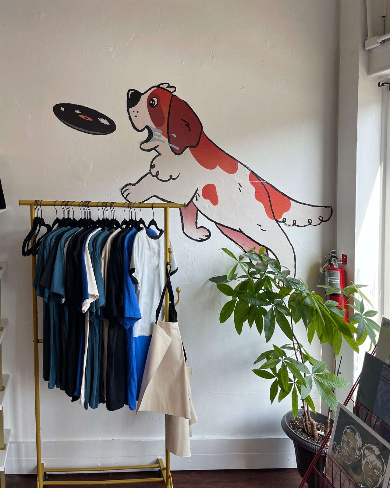 The spaniel mascot painted on an interior wall, leaping to catch a vinyl record above a rack of shop tees and totes