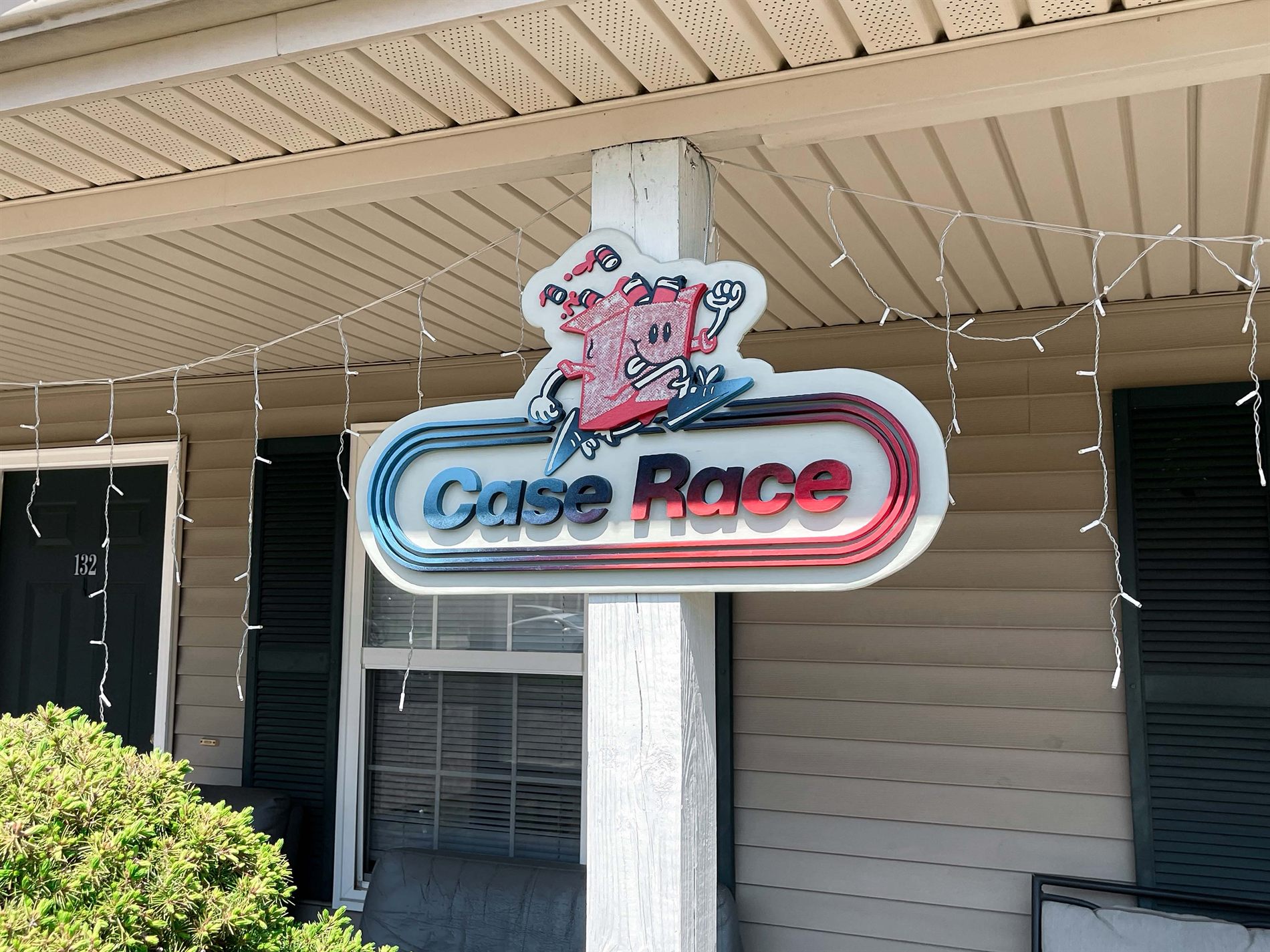 Layered Case Race sign with a sprinting beer case mascot, mounted on the front porch post of the house
