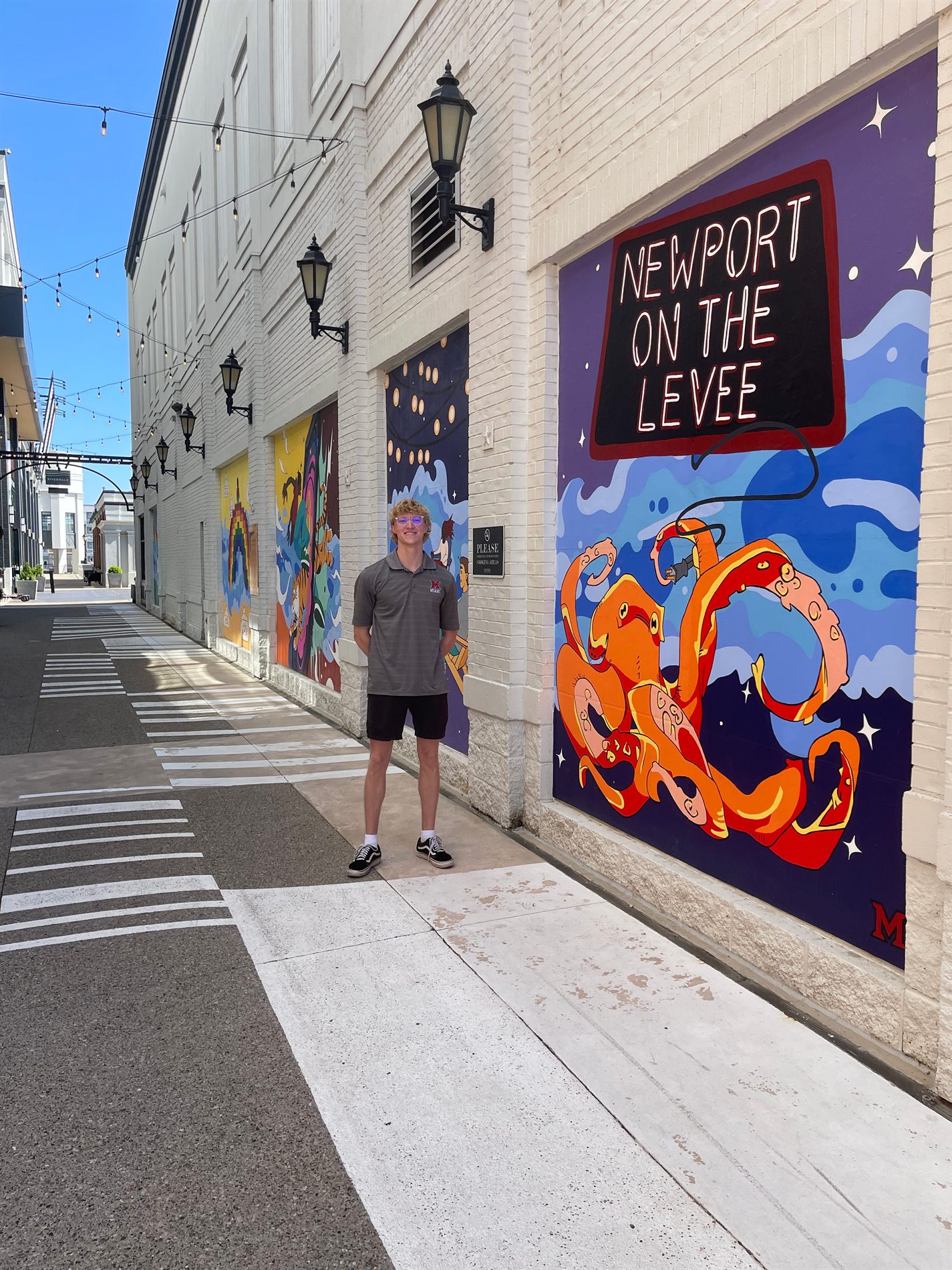 The finished Newport on the Levee mural panels running along the walkway, with a painted neon sign and an orange octopus in blue waves
